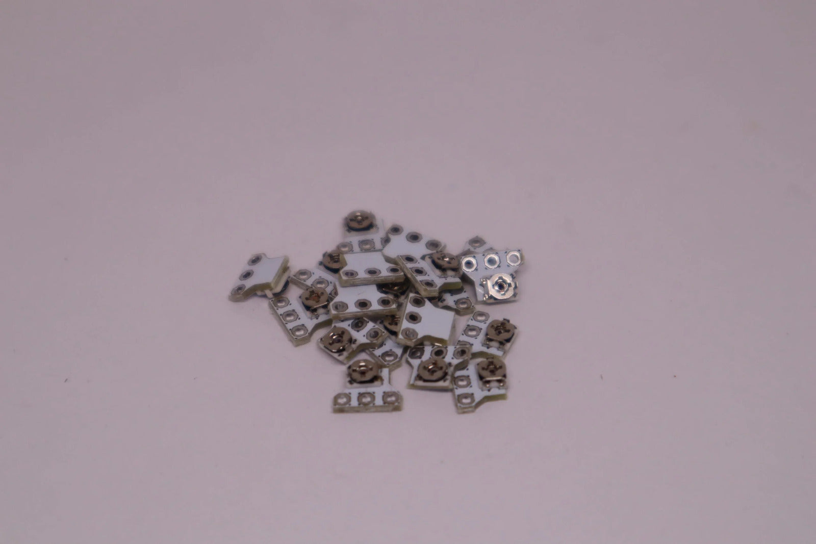 Ein kleiner Haufen metallischer Stick neu kalibrieren Modul-Komponenten ist auf einer hellrosa Oberfläche verstreut und erinnert an die winzigen Teile im Inneren eines PS5-Controllers.